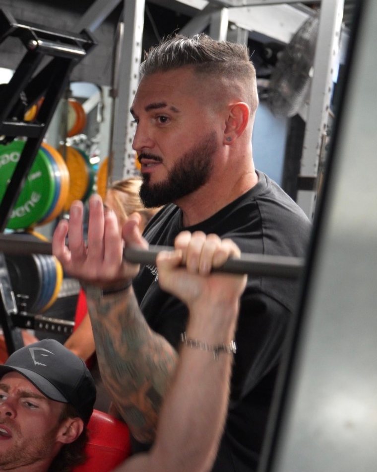 Robbi, head coach at Goatlifters, spotting Sam in the gym